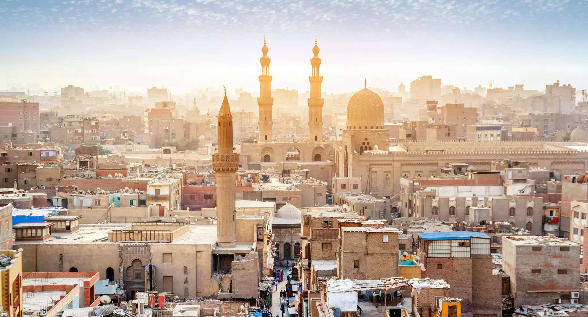 Minarets and other towers rise over sand-colored buildings under pale blue sky in Cairo, Egypt.