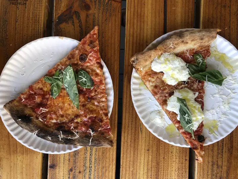 Pizza slices from L'Industrie on paper plates and resting on a wooden table
