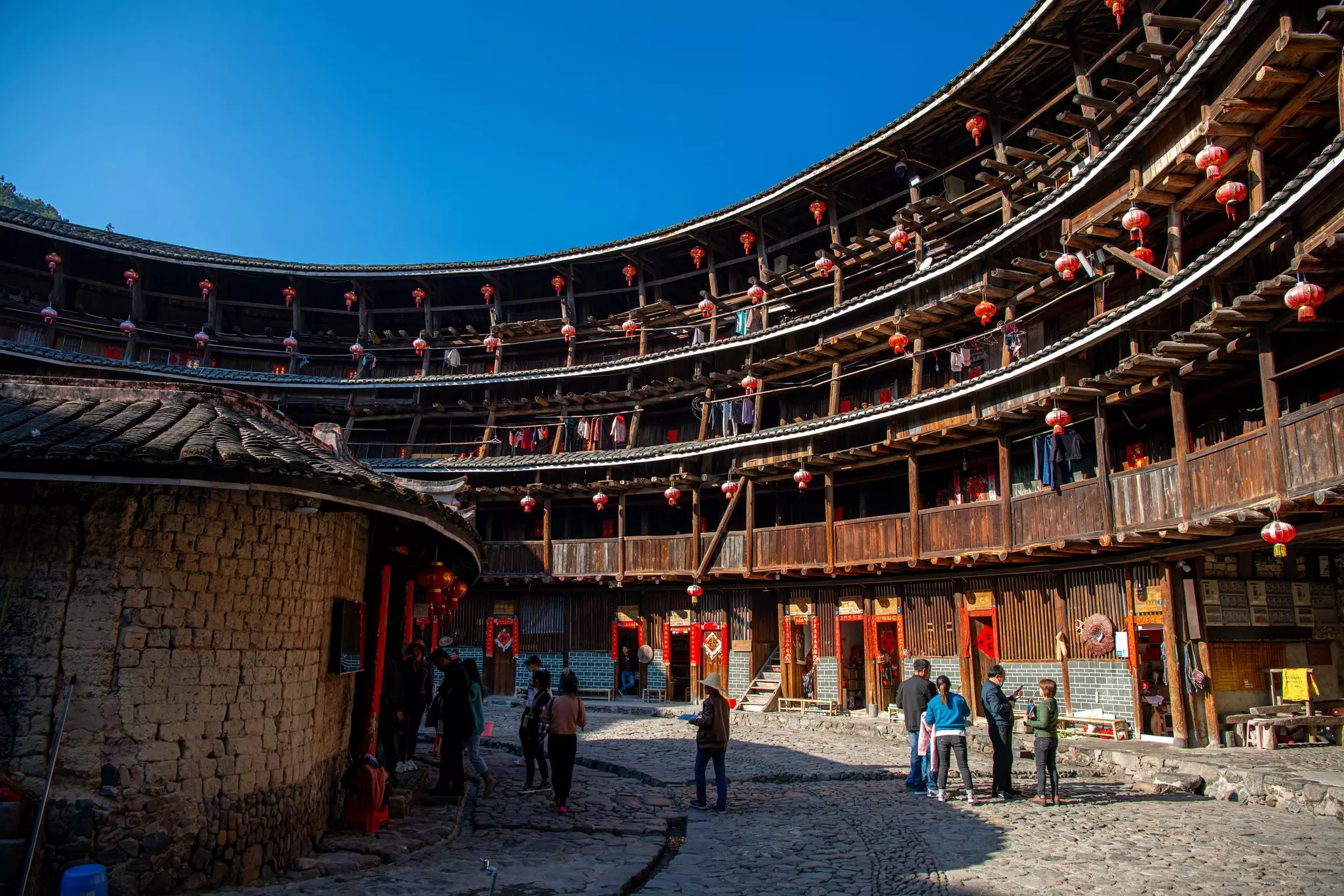 People walk the perimeter of of a historic circular building, whose interior stories are lined with wooden columns and banisters.
