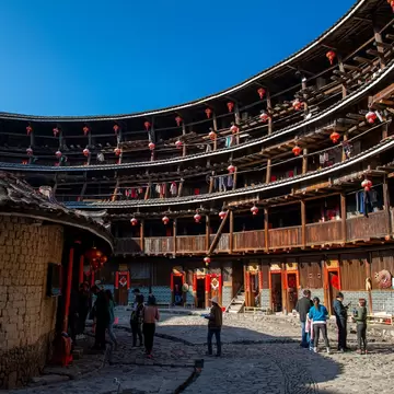 People walk the perimeter of of a historic circular building, whose interior stories are lined with wooden columns and banisters.