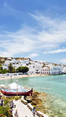 A boat sits in a turquoise harbor with whitewashed Greek buildings in the background. 