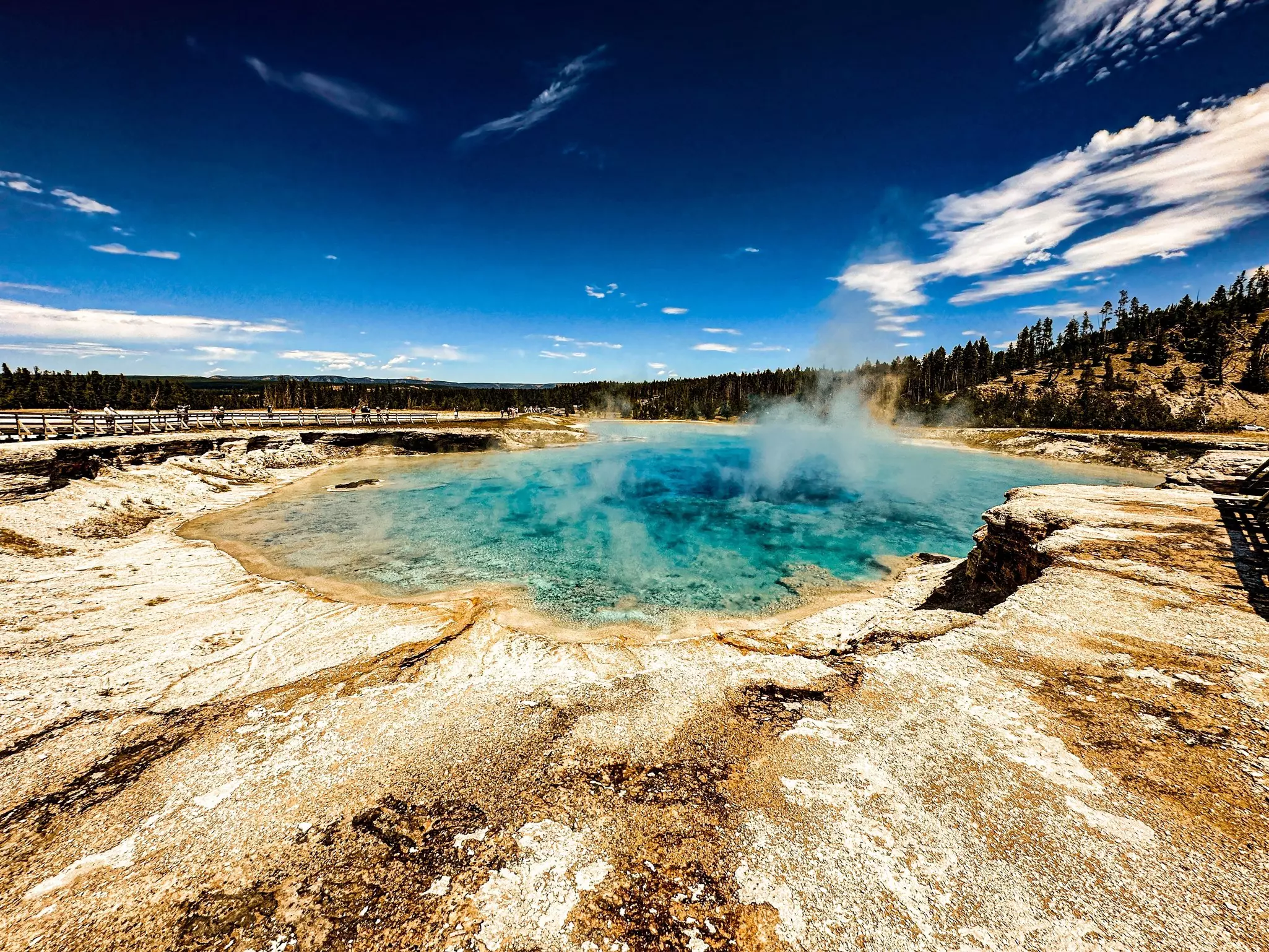 Walkers gaze at a translucent blue pool of steaming water from a safe distance on a summer's day