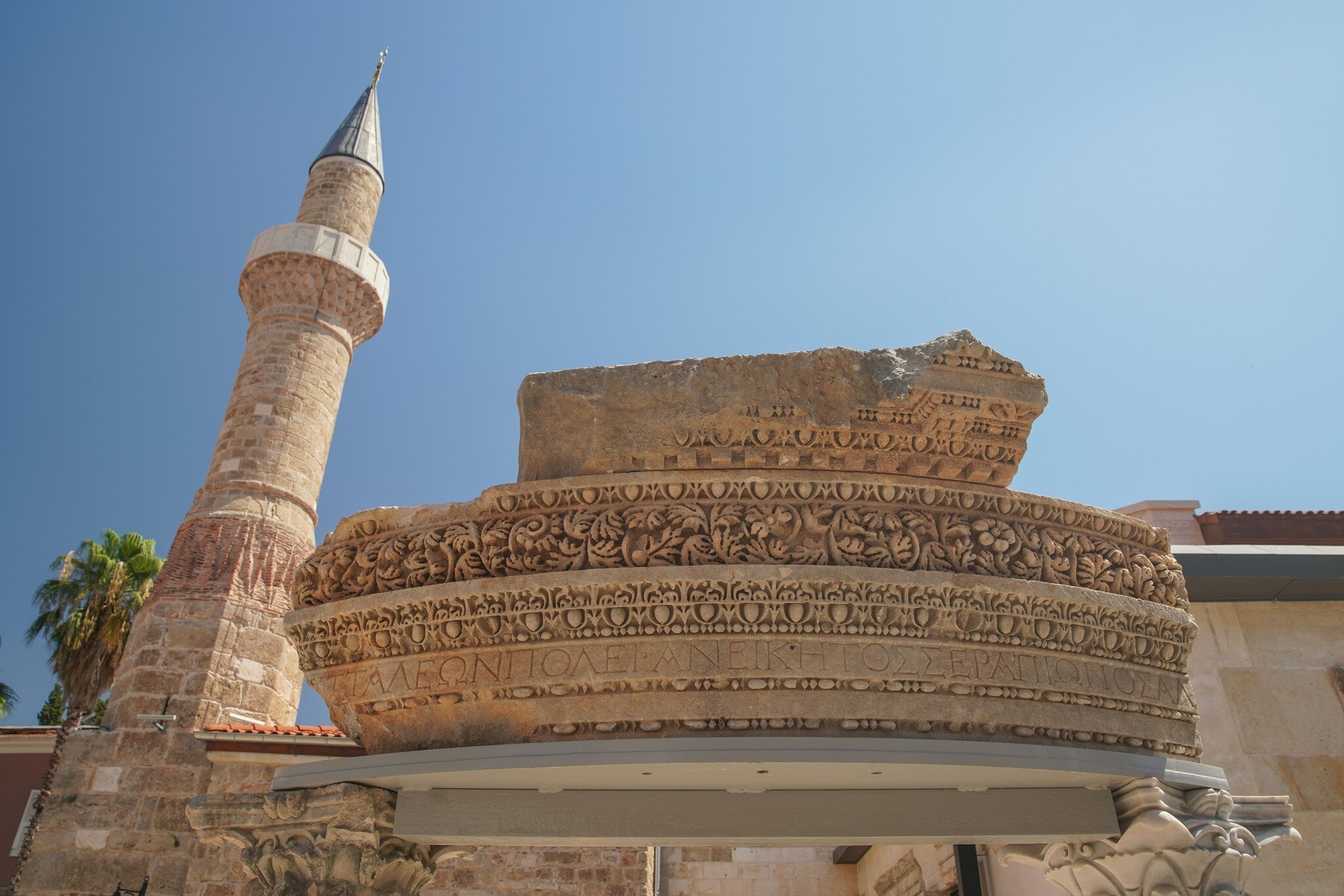 Stone minaret in Antalya rising behind a Roman cornice fragment inscribed in Greek with the ancient city name of Attaleia