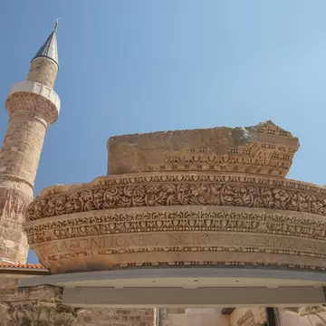Stone minaret in Antalya rising behind a Roman cornice fragment inscribed in Greek with the ancient city name of Attaleia