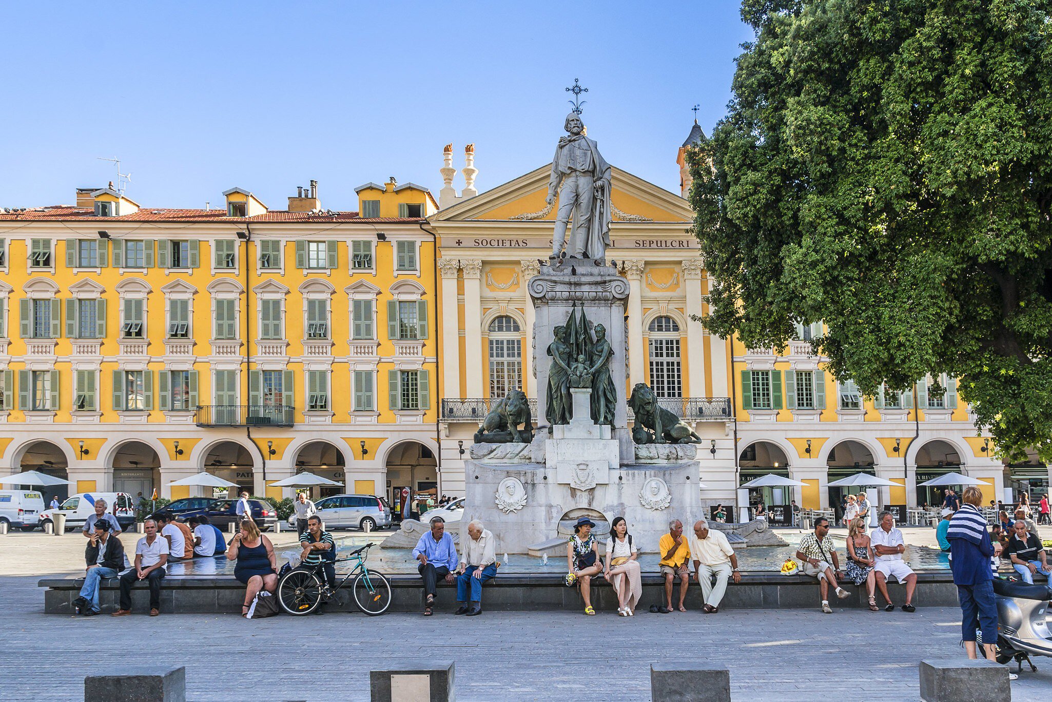 Row of people sit around the Statue of Garibald at Place Garibaldi (town square) in Nice, France.