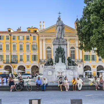 Row of people sit around the Statue of Garibald at Place Garibaldi (town square) in Nice, France.