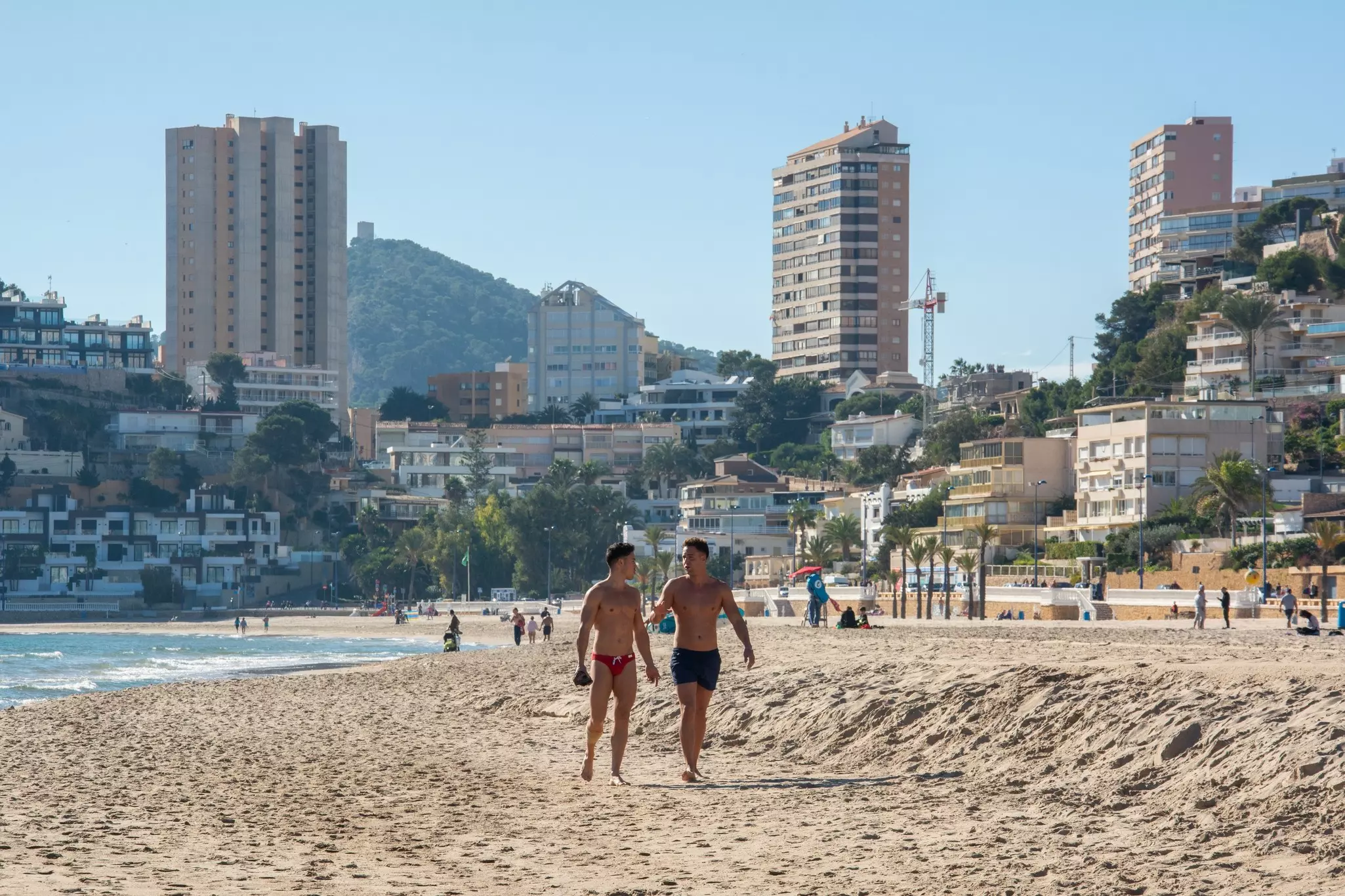 Two men walking along the beach in Benidorm, Costa Blanca, Spain.