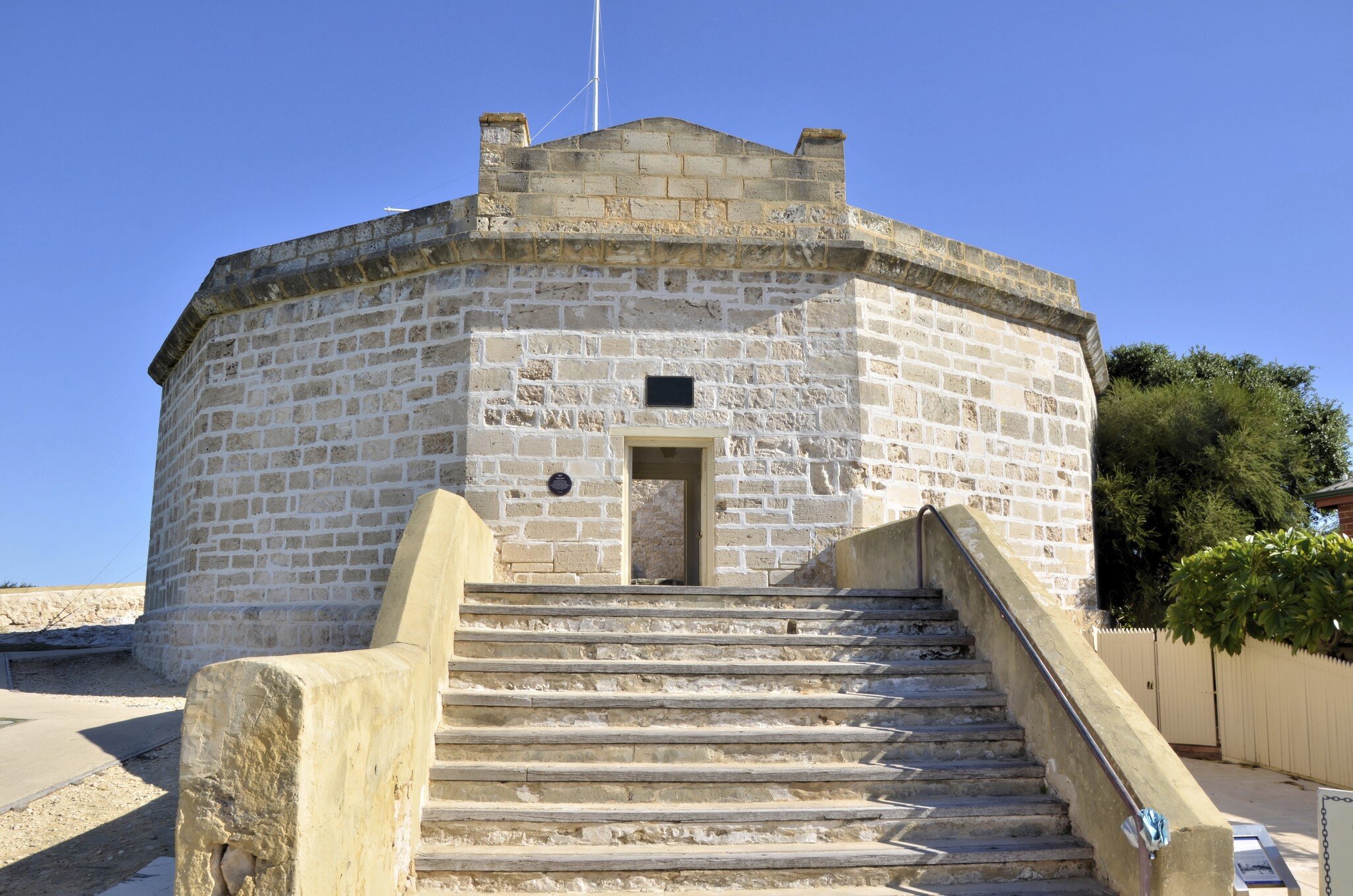 Pale limestone building with many sides and an open doorway, reached by a broad flight of stone steps under a blue sky