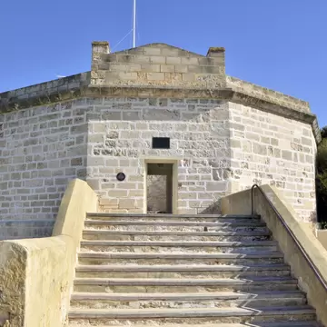 Pale limestone building with many sides and an open doorway, reached by a broad flight of stone steps under a blue sky