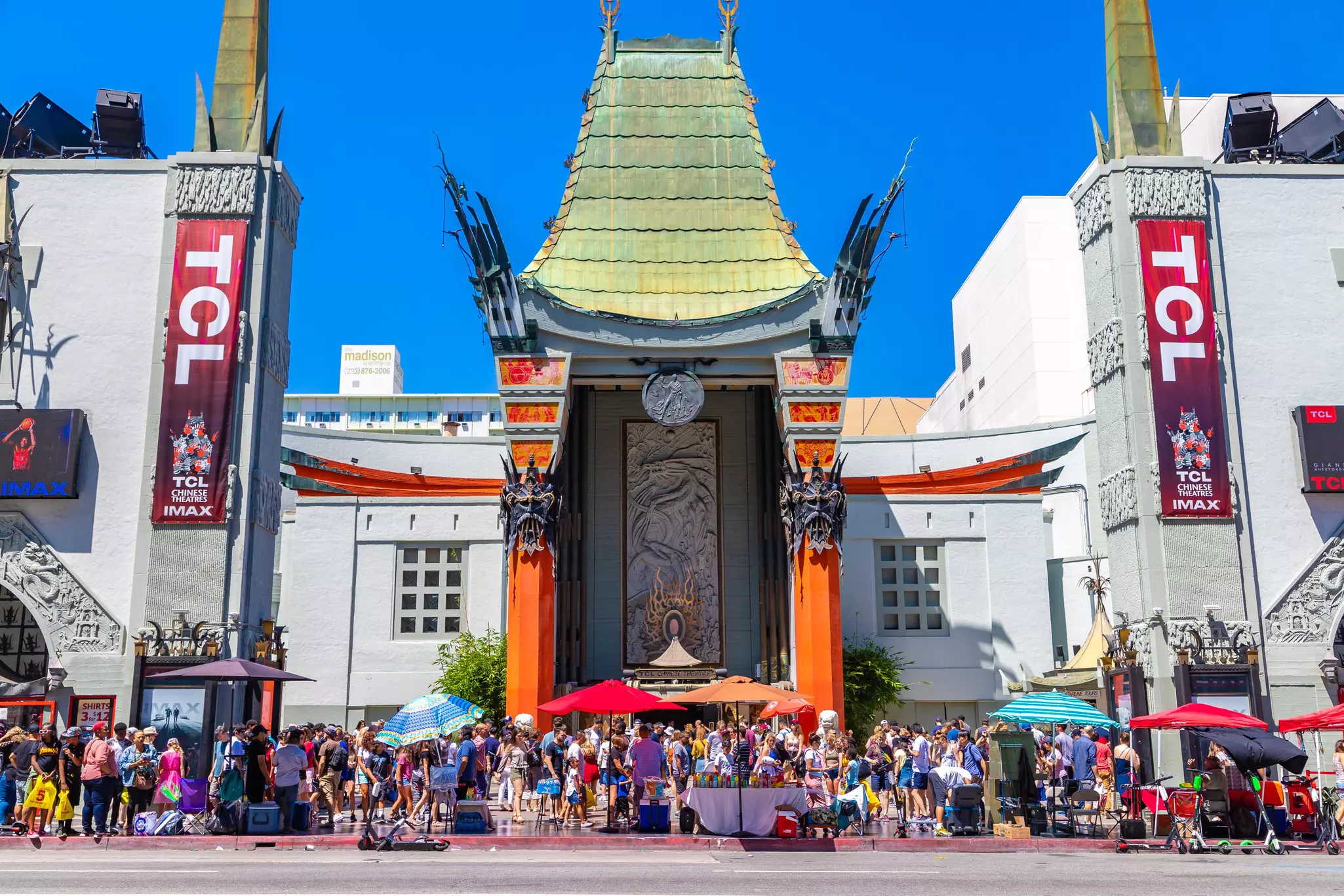 People dressed casually on a sunny day move around outside a Chinese-style building on a busy sidewalk.