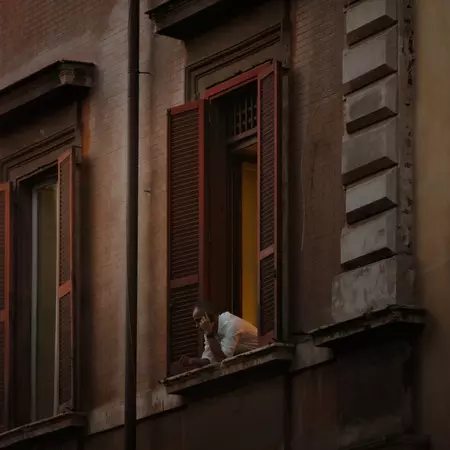A man looks out over his open window from a typical Roman apartment building