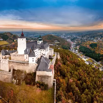 Burg Forchtenstein castle in Burgenland: white tower with red cap and stone ramparts on a wooded ridge, village in the valley