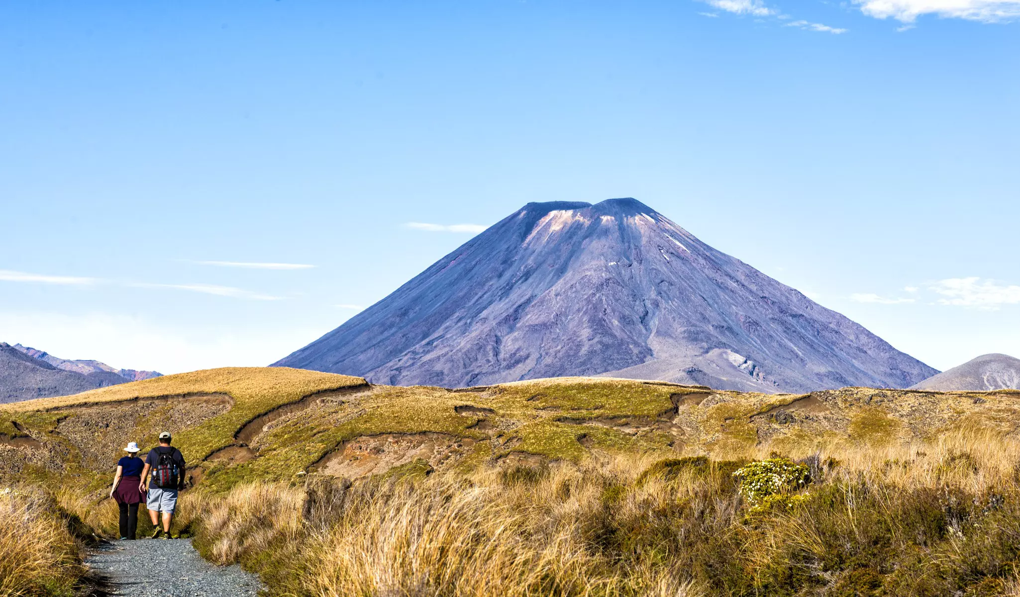 Two hikers walking on a stony trail near a volcanic peak