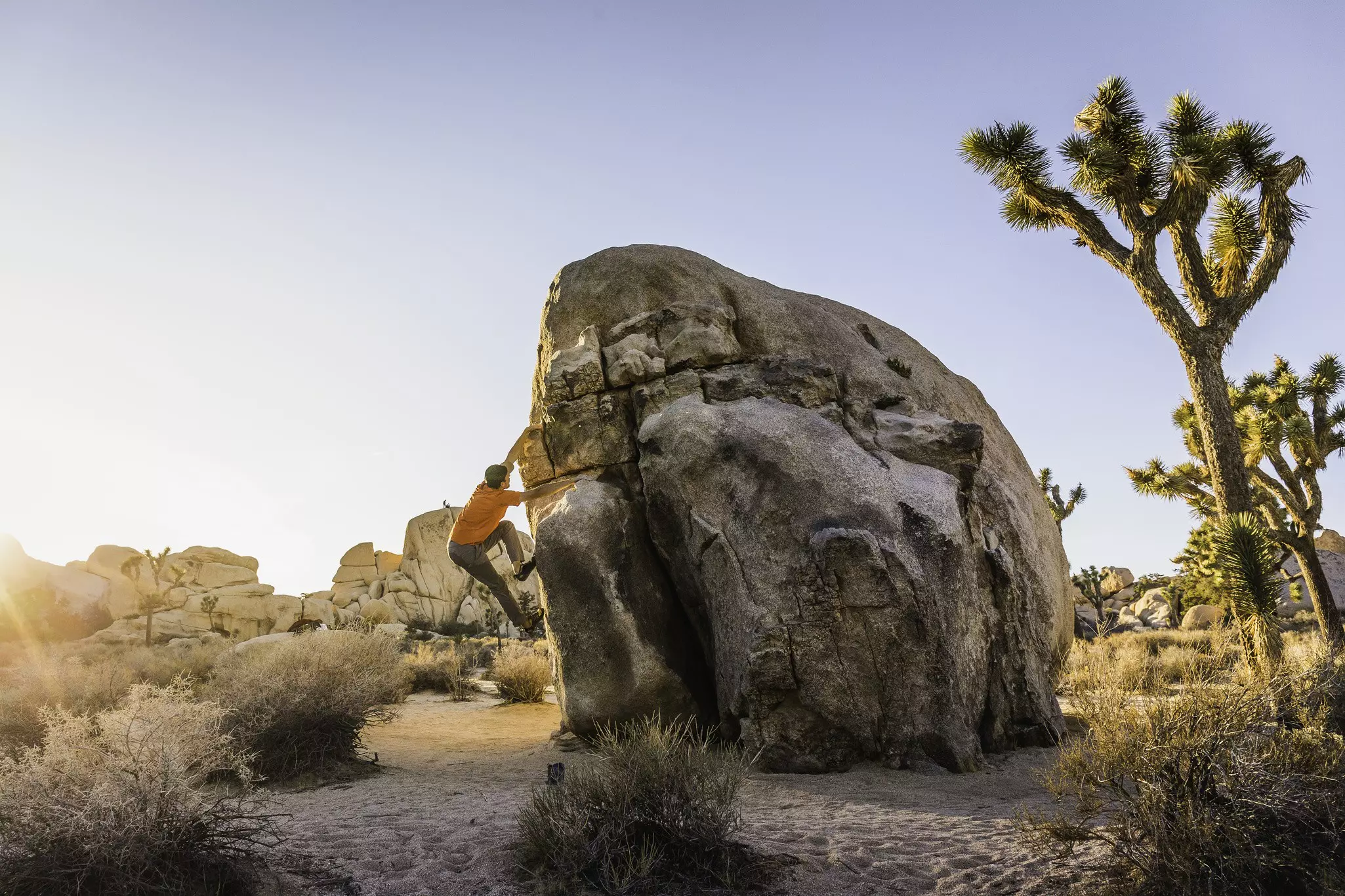 Male boulderer moving up a freestanding boulder at dusk
