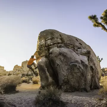 Male boulderer moving up a freestanding boulder at dusk
