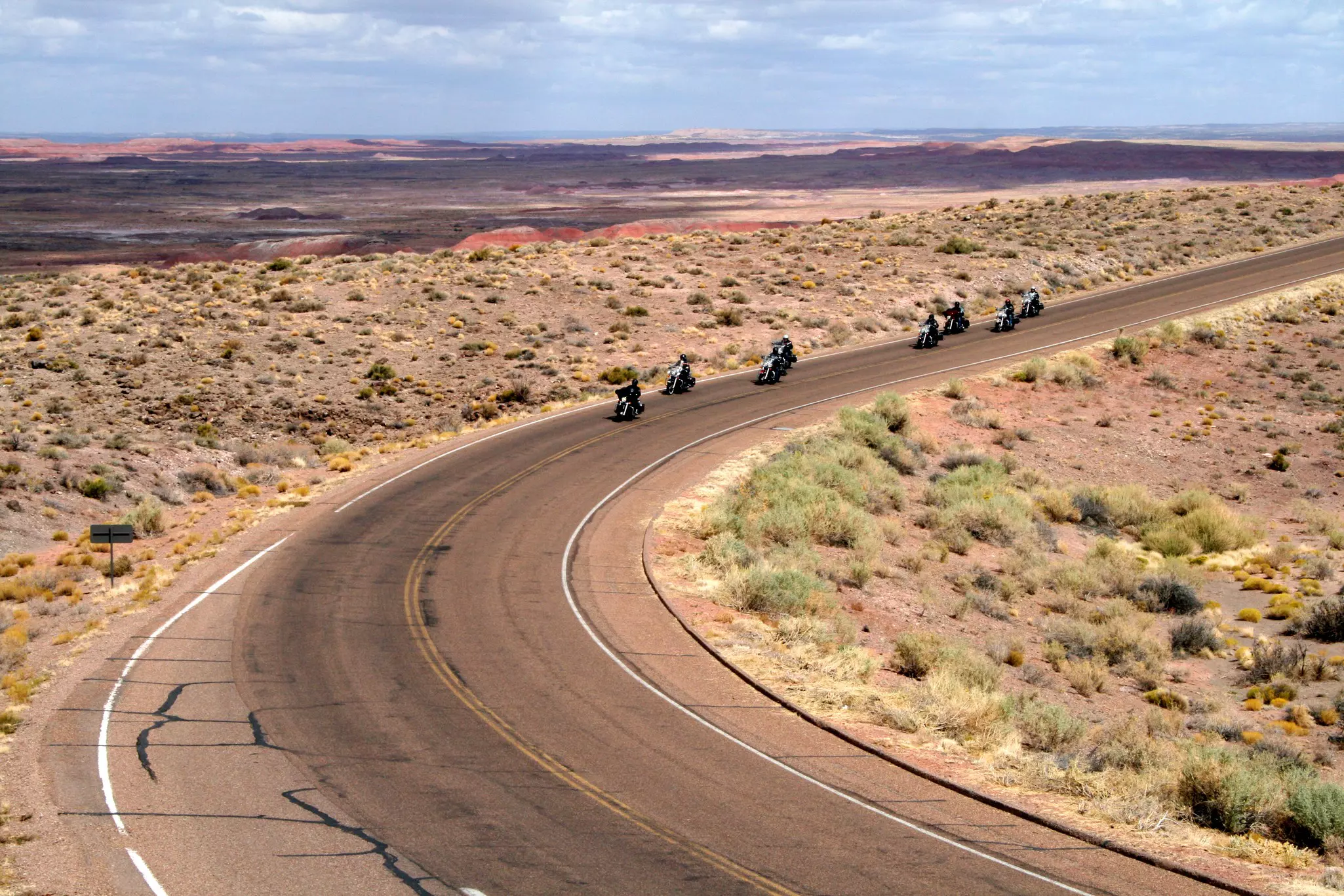 A group of motorcyclists approach a curve along a desert highway.