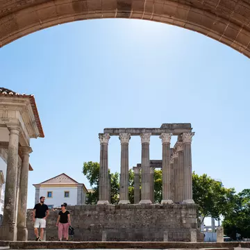 Two people walk by the ruins of a Roman temple in a town