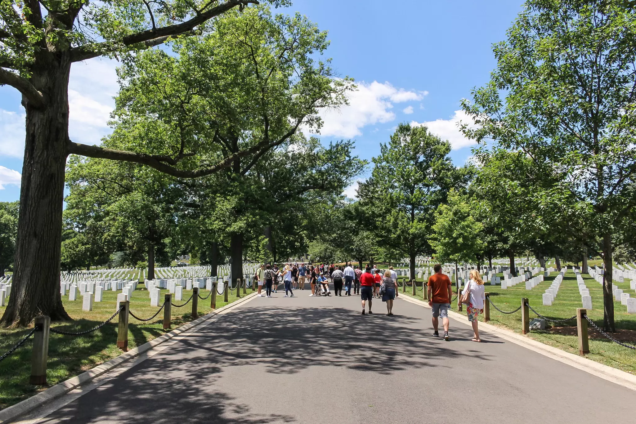 People walk down the paths through the cemetery on a sunny day.