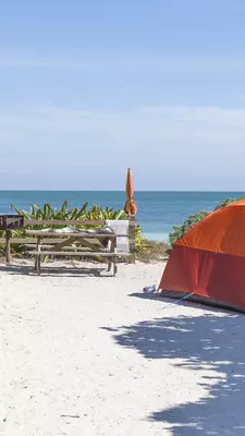 A tent on a beach beside a picnic table with the ocean in the background 