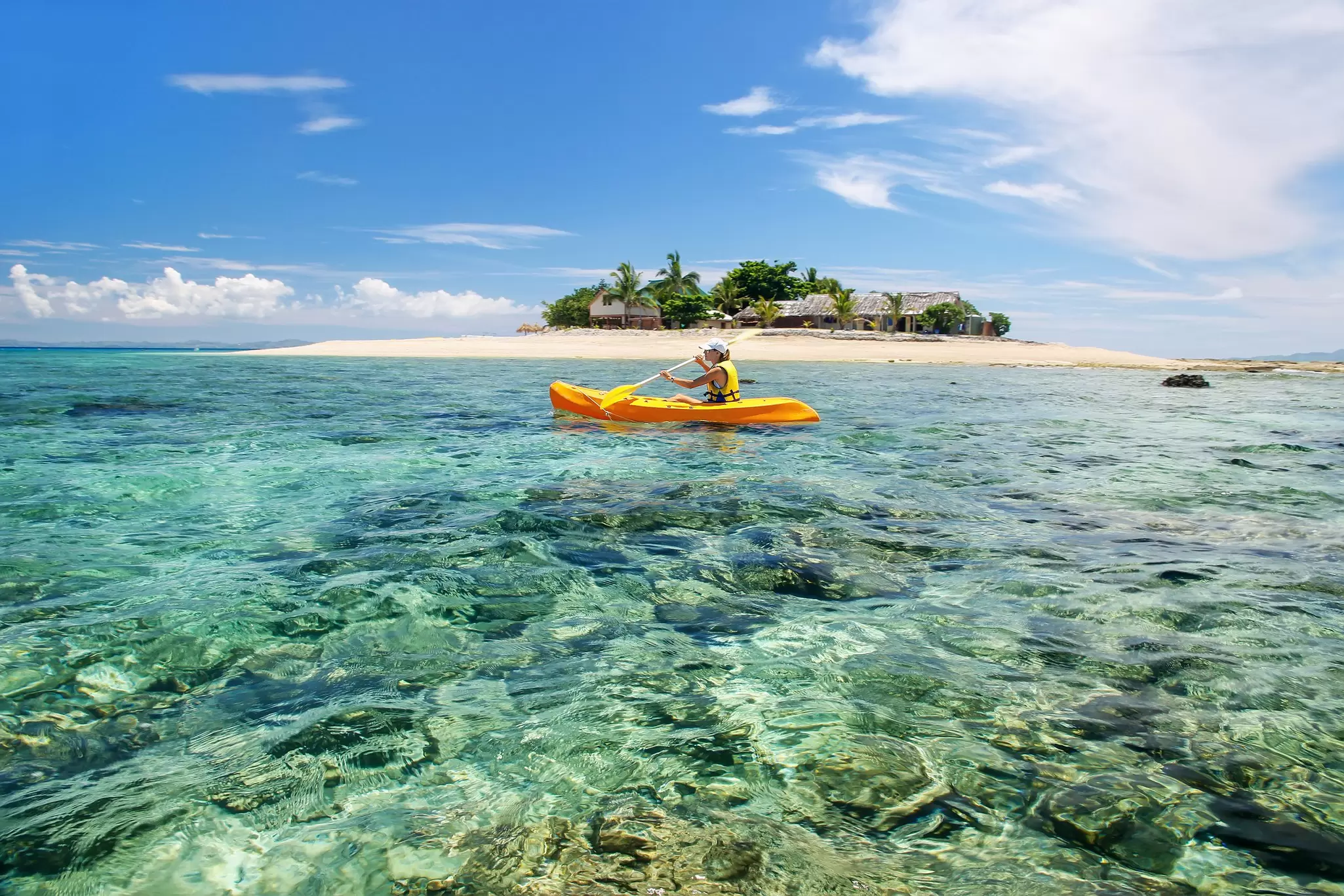 A woman in a yellow kayak on clear waters with a small island behind her