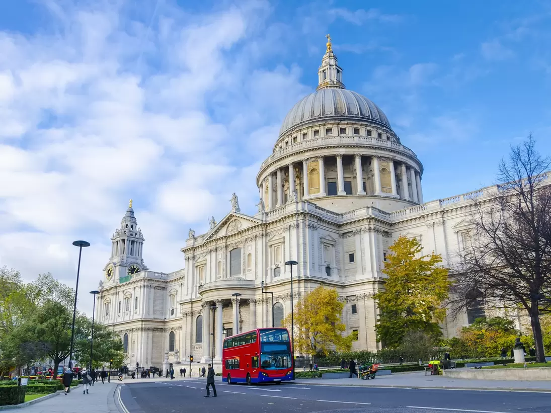A red double-decker bus passes in front of a large domed cathedral