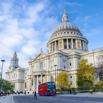 A red double-decker bus passes in front of a large domed cathedral