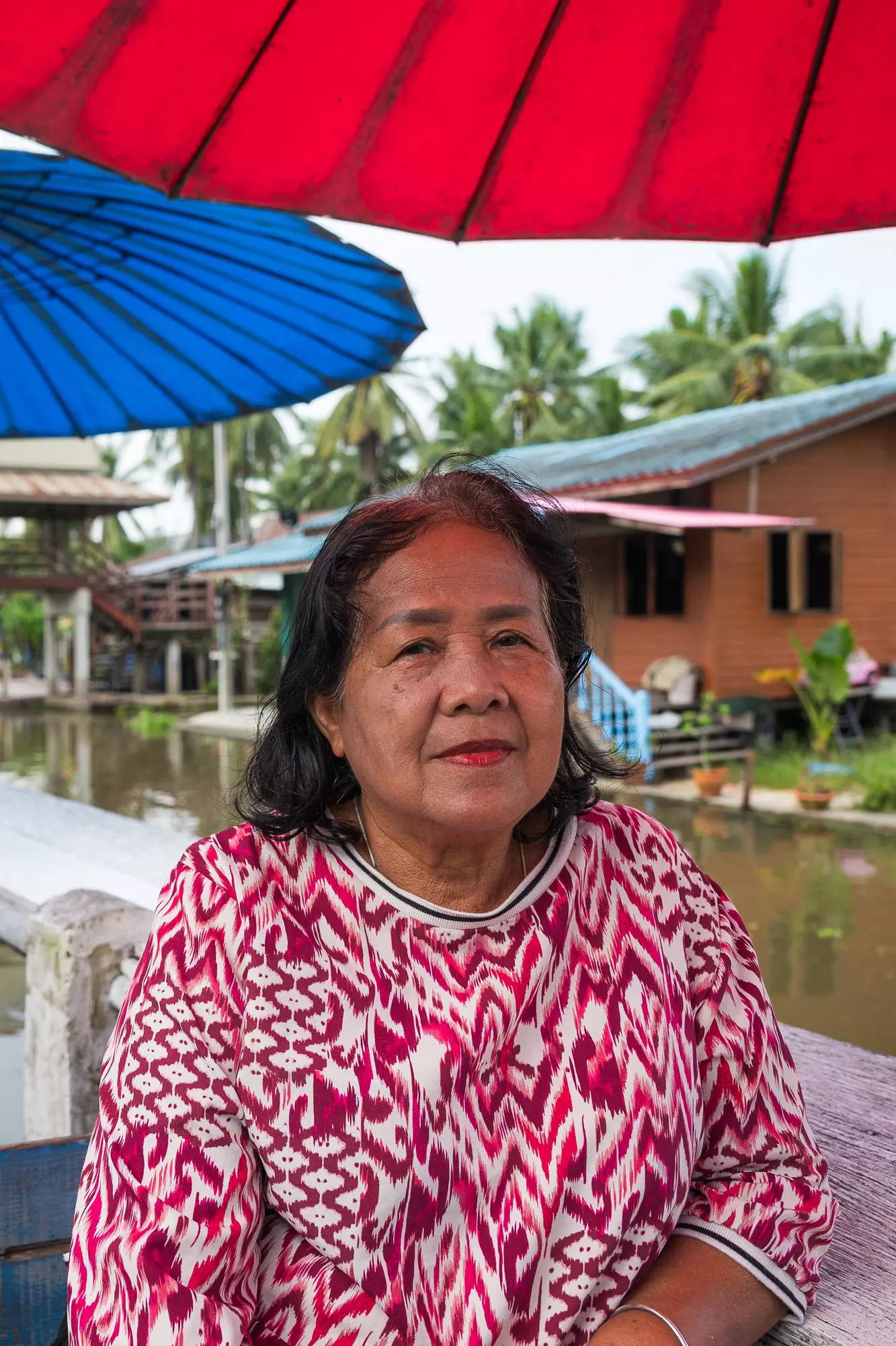 A woman in a brightly printed shirt looks into the camera aboard a boat in a canal.