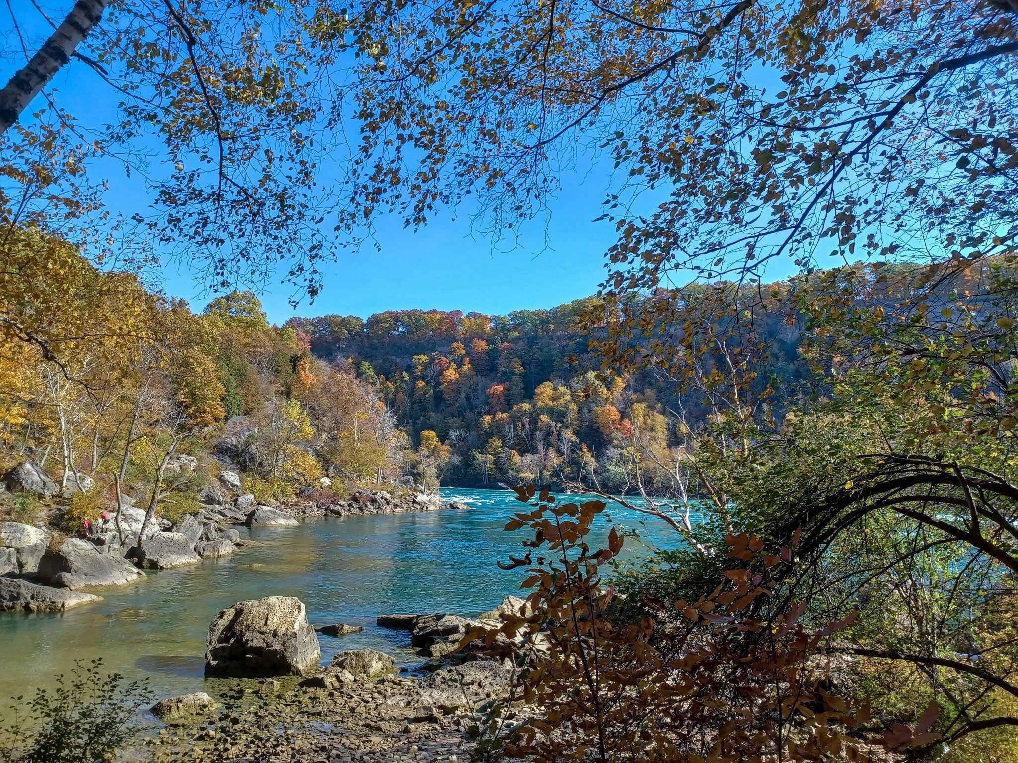 A bend in a turquoise-colored river in Ontario, Canada, is seen from a rocky shore in autumn.