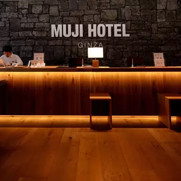 The large, wooden reception desk at a hotel with its name, "The Muji Hotel," in block letters on the wall behind it
