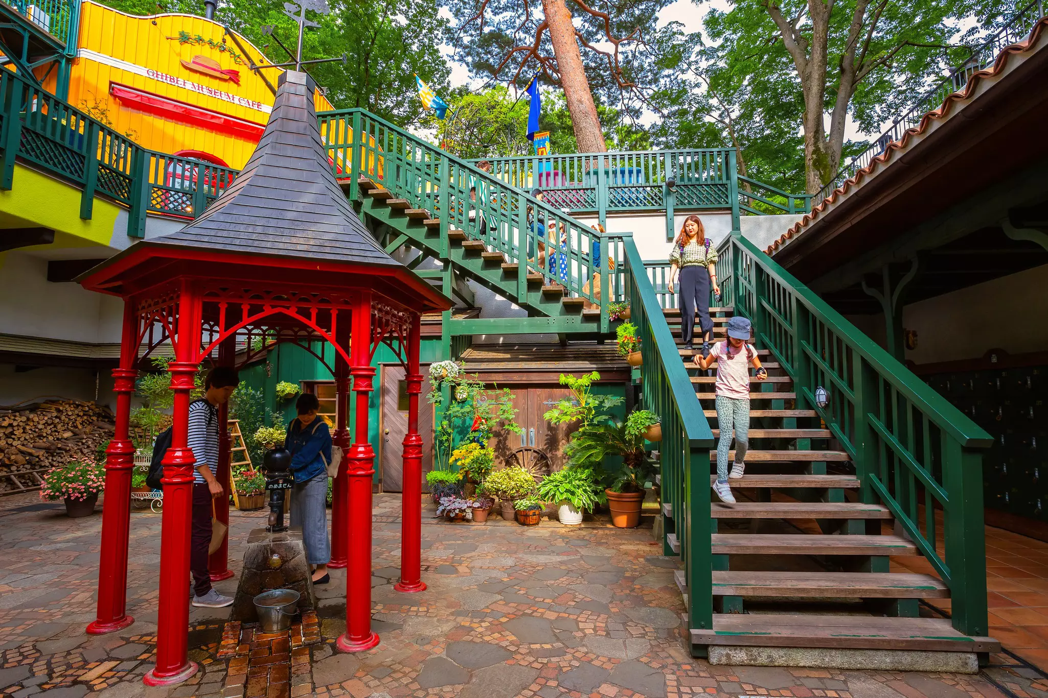 A child walks on a wooden staircase next to a red gazebo in the garden of a museum complex.