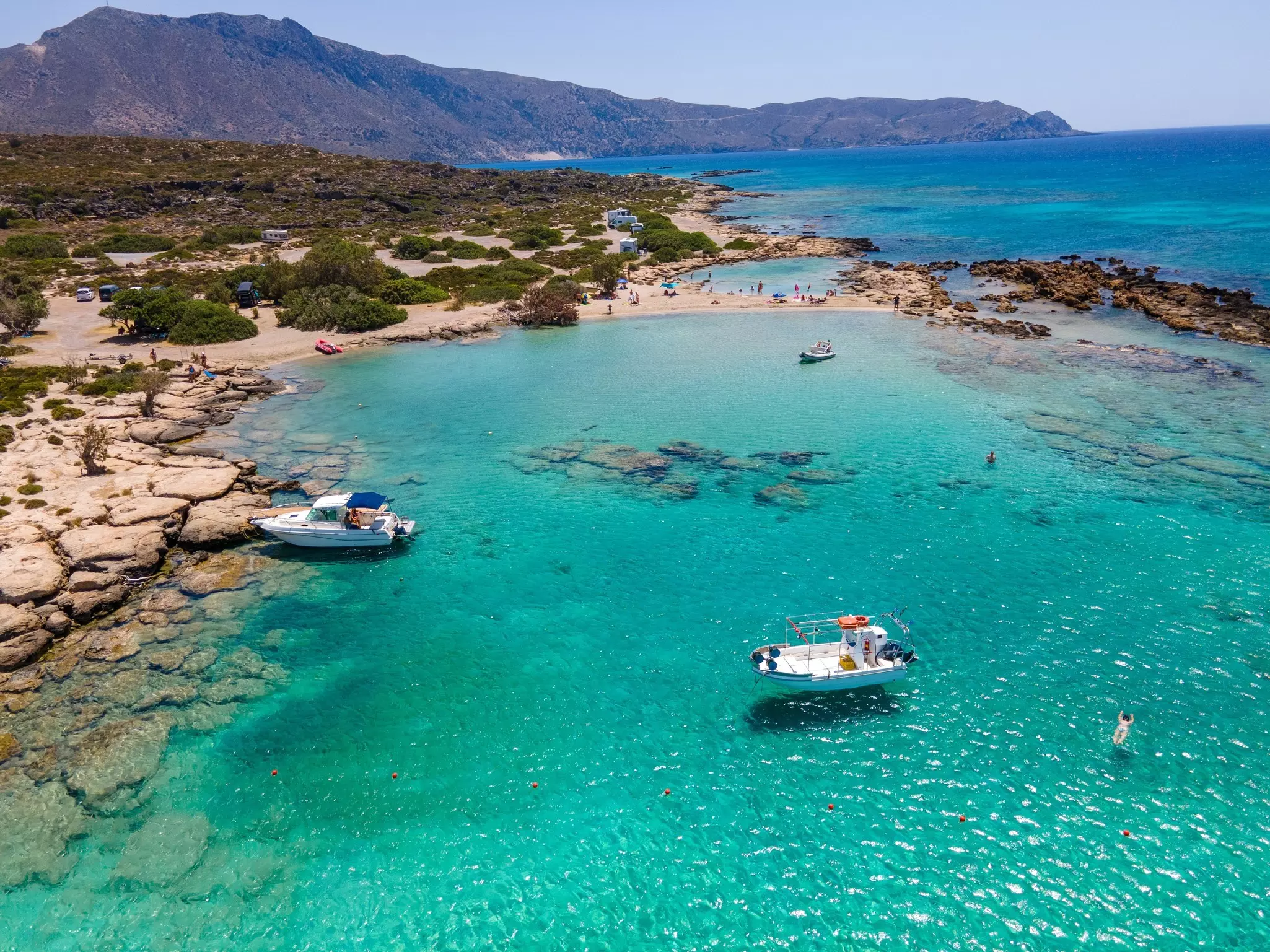 Two boats in a turquoise cove with a narrow strip of pinkish sand.