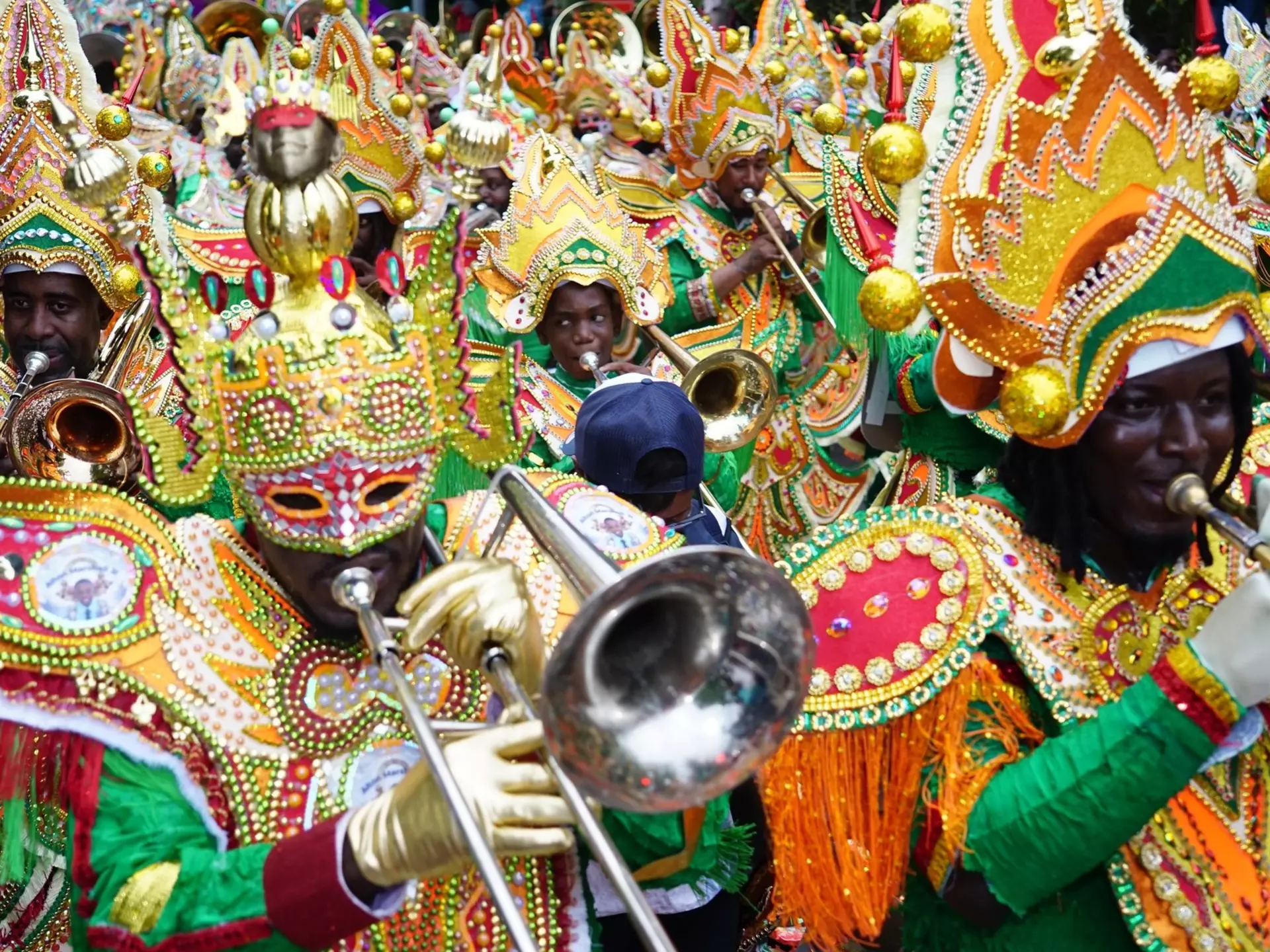 People in elaborate, colorful beaded costumes play brass instruments as part of a cultural festival.