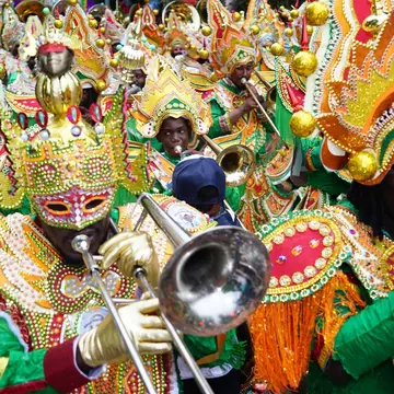 People in elaborate, colorful beaded costumes play brass instruments as part of a cultural festival.