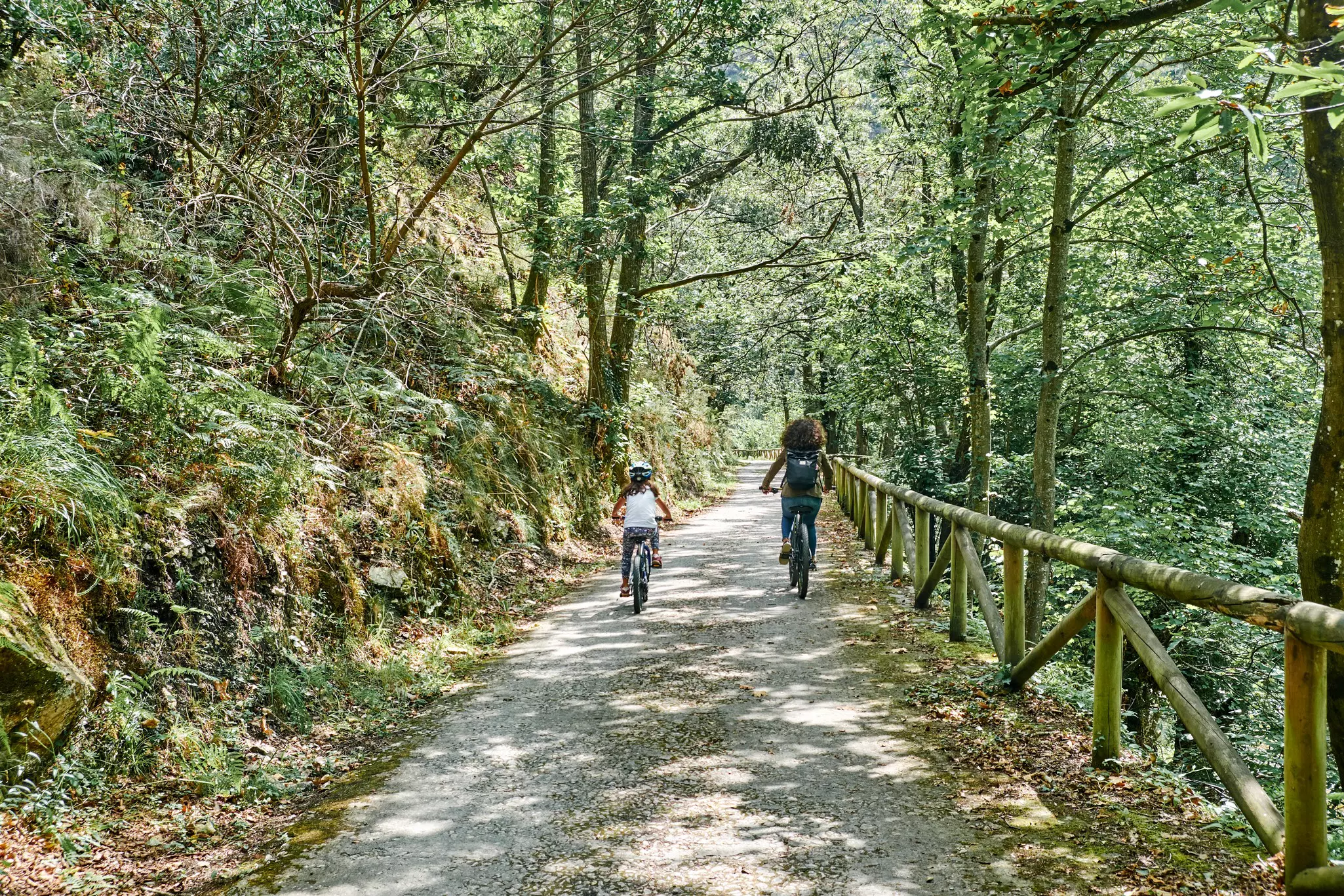 A woman and child cycle in the dappled light on the Bear Path (Senda del Oso) in Asturias, Spain