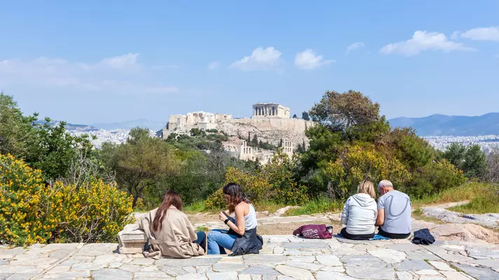 Athenians relaxing at Filopappou Hill enjoying the view of Acropolis Hill with Parthenon temple on top.