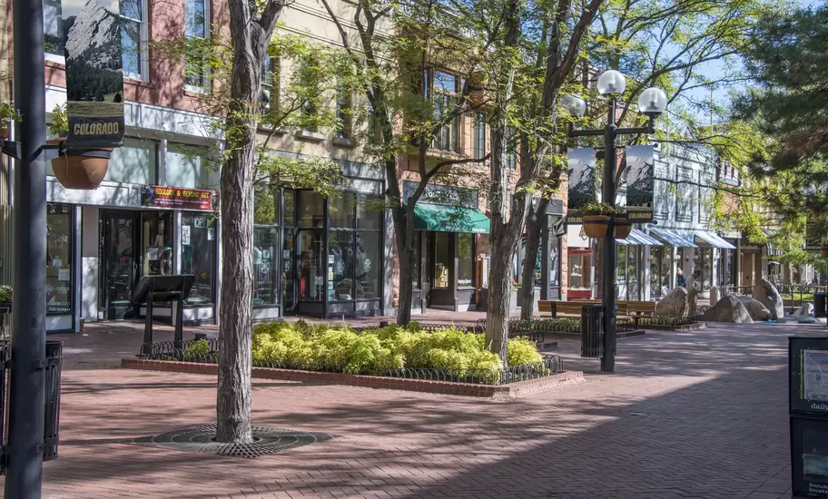 Pedestrian mall in Boulder, Colorado, with brick paving, trees, shopfronts and Colorado banners showing the Flatirons