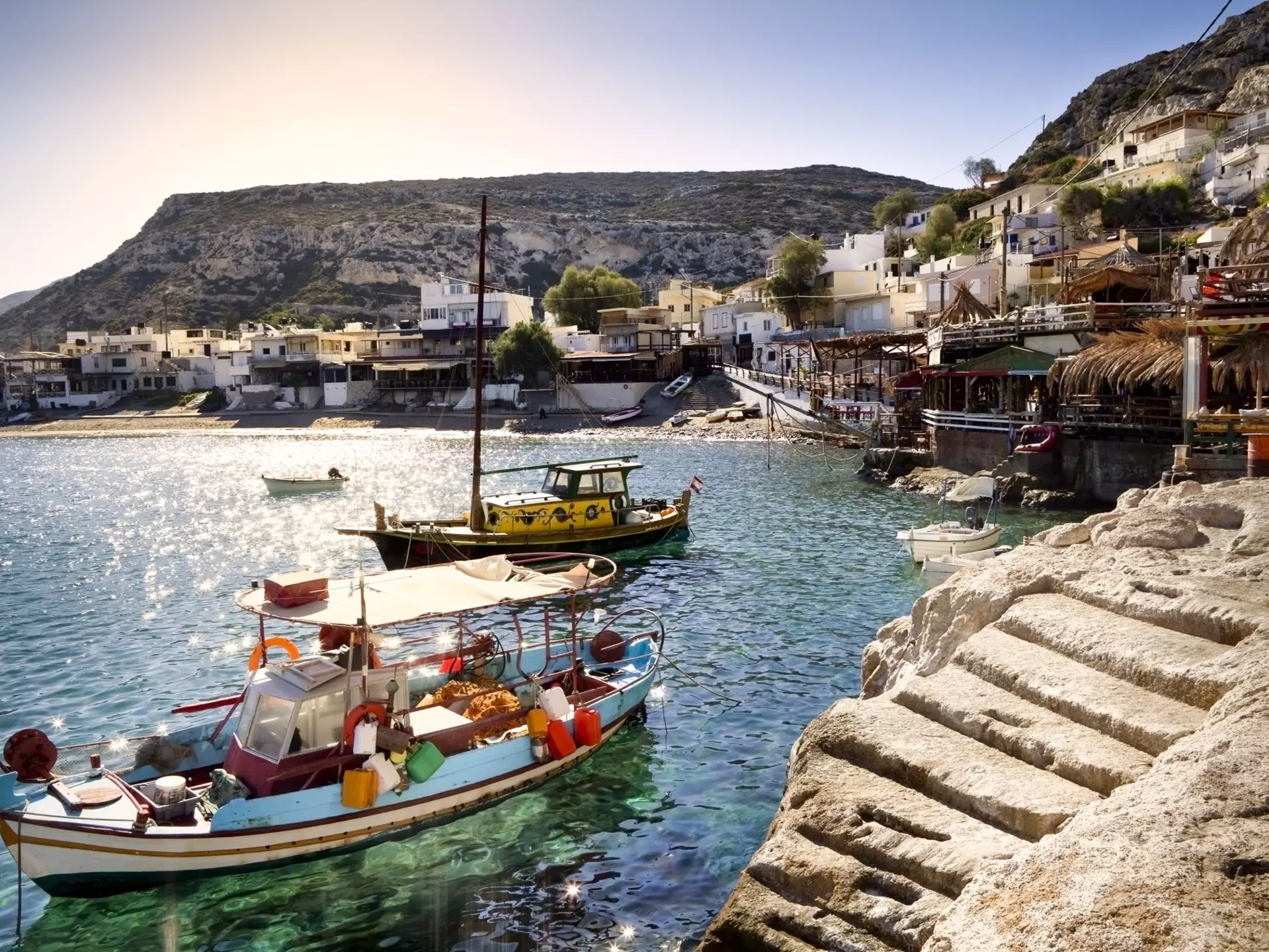 A few fishing boats moored in Matala (on Crete island in Greece) at sunrise. Bars, restaurants and hotels in the background. 