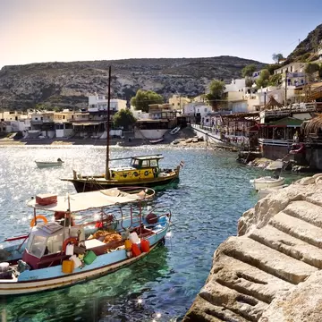 A few fishing boats moored in Matala (on Crete island in Greece) at sunrise. Bars, restaurants and hotels in the background. 