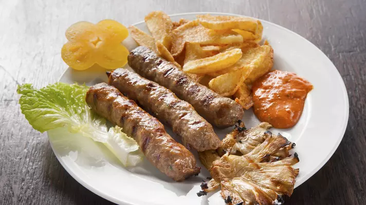 Three oblong meat patties on a plate with a leaf of green lettuce, a reddish sauce and potato chips.