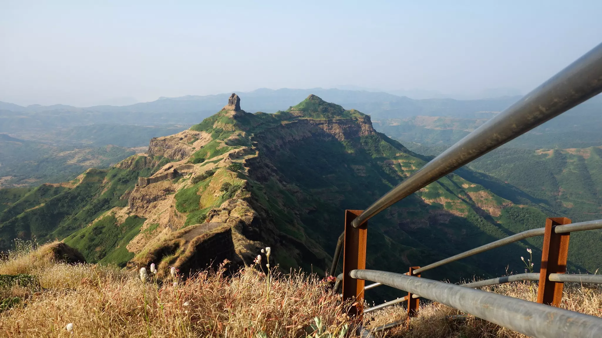 The fence lining a pathway on a hilltop ridge leading to a ruined fort, with expansive views beyond.