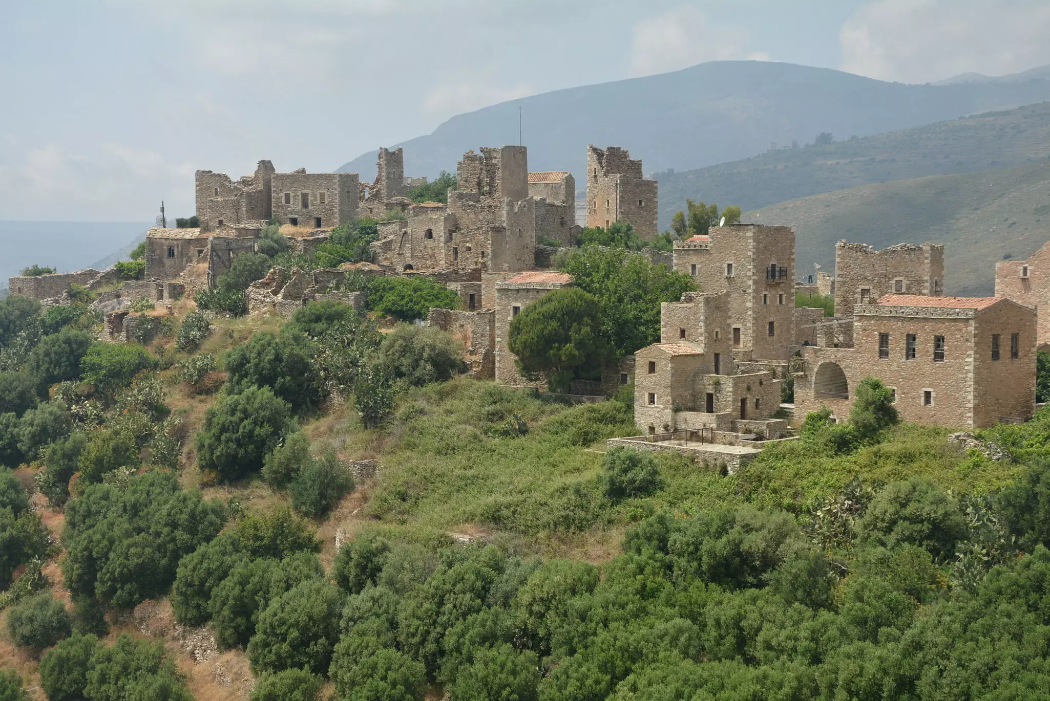 View of the stone buildings of the Vathia tower houses in the Mani region of Peloponnese. Some of the buildings are crumbling on the green mountainside.