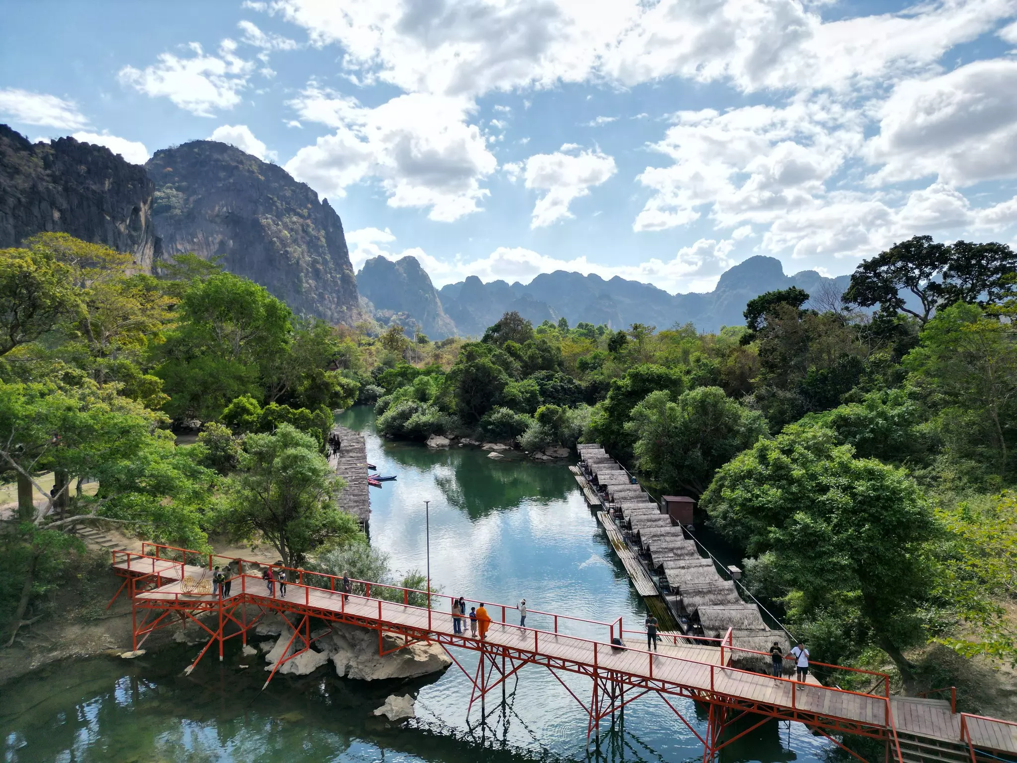 A bridge over a river near a majestic mountain range surrounded by jungle.