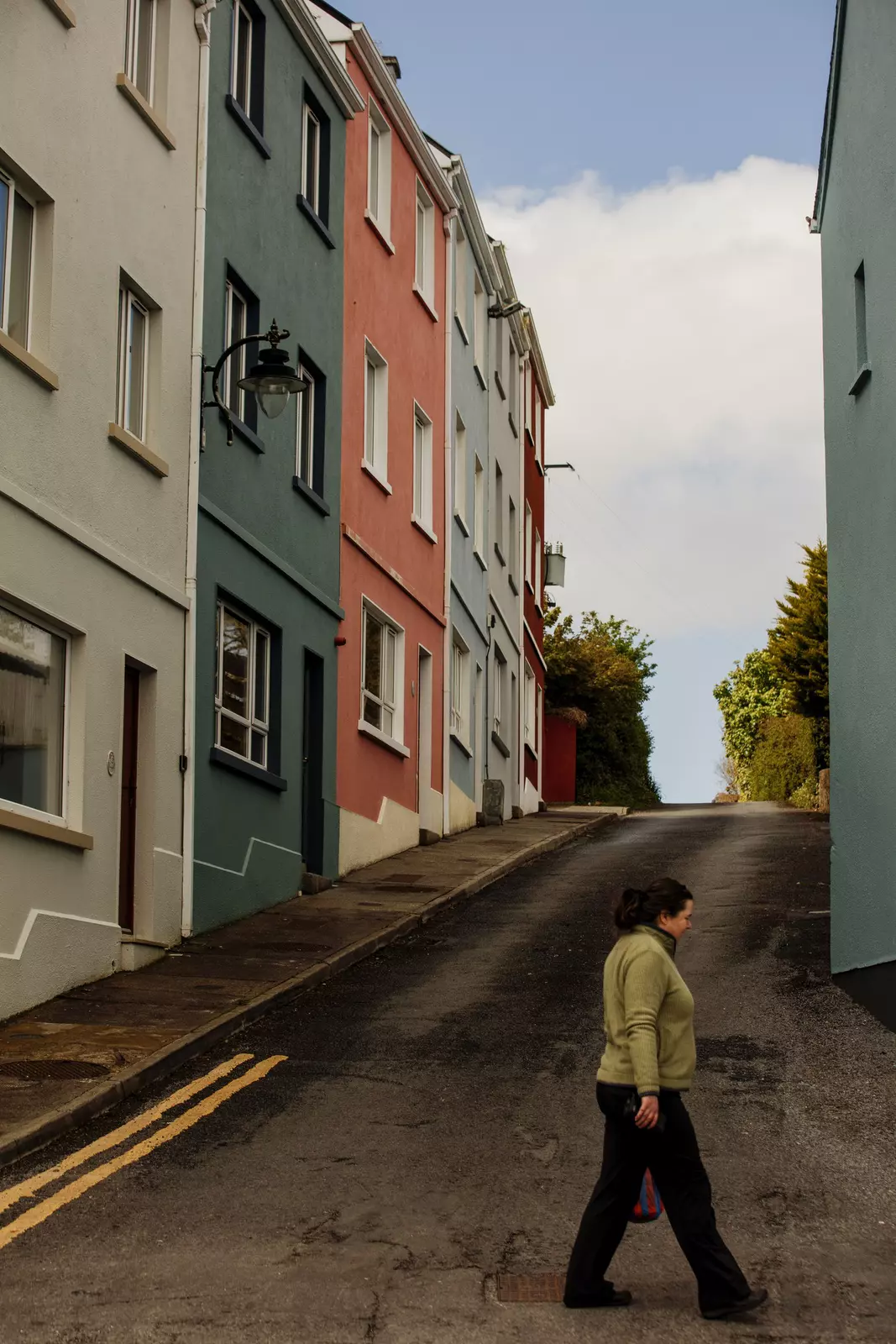 A woman crosses a street lined with colorful houses. Roundstone is a village on the west coast of Ireland, in the Connemara region of County Galway, Ireland