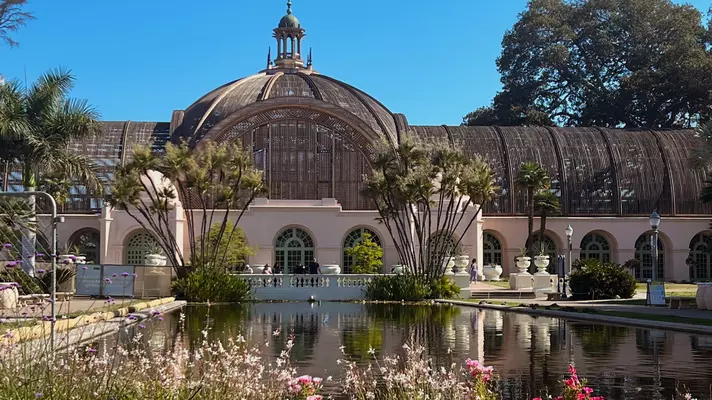 A botanical building with a rectangular pool in front on a sunny day.
