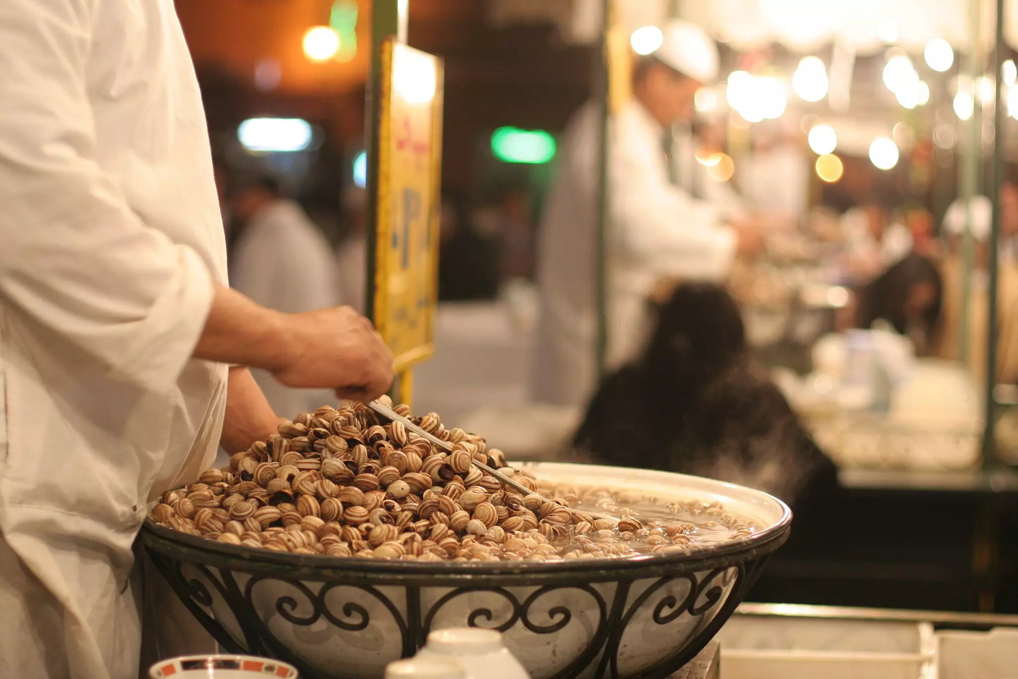 A pair of hands stirs snails in a large bowl at a food stall in Morocco