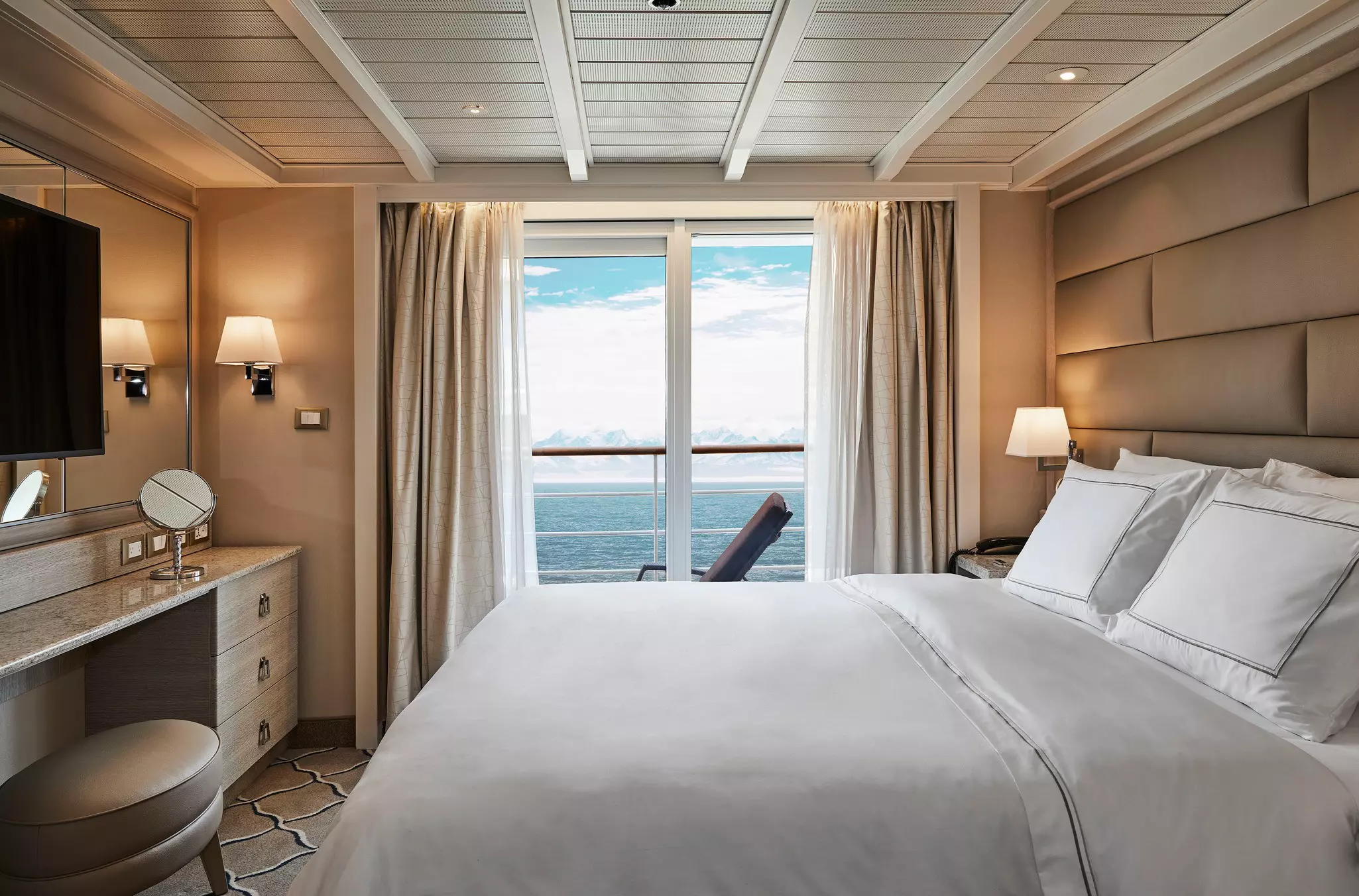 A bedroom on a cruise ship with a deck offering views of a snowcapped mountains and icy ocean.
