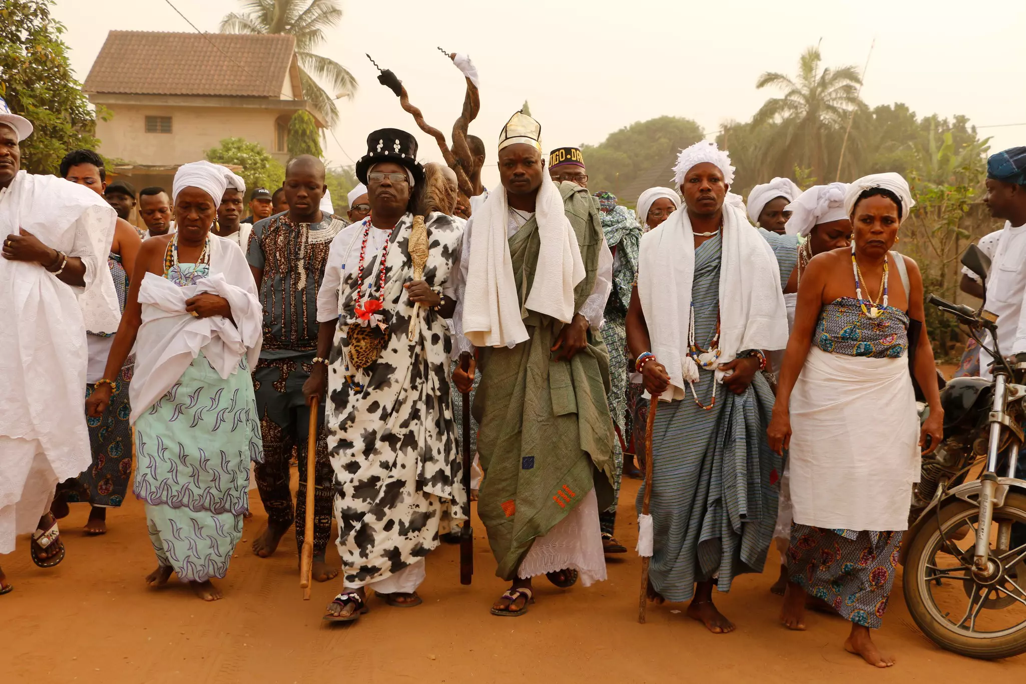 People in long tunics and white cloths walk side by side down a street during a religious festival.