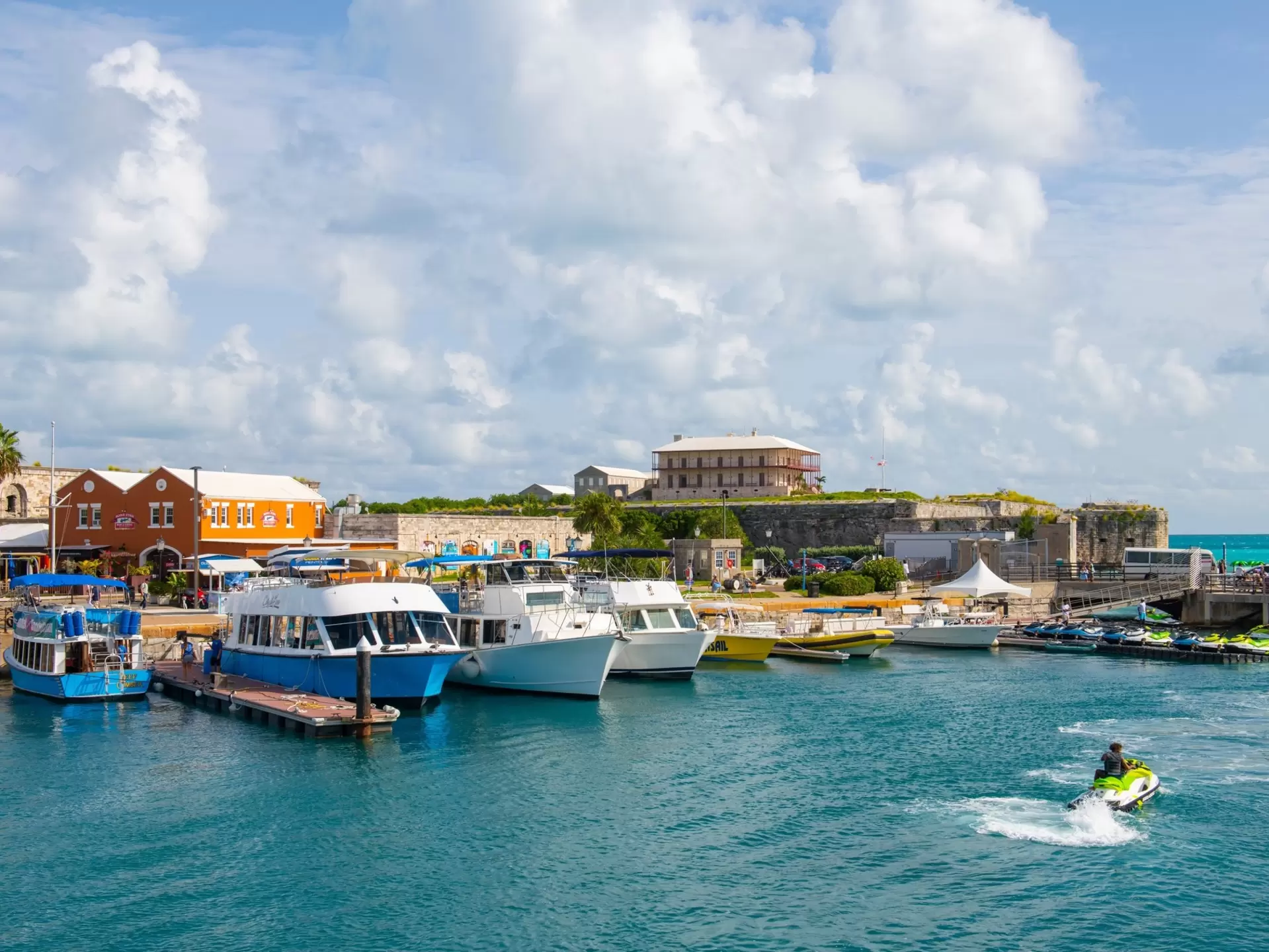 Boats moored at a marina as a person passes by on a jet ski