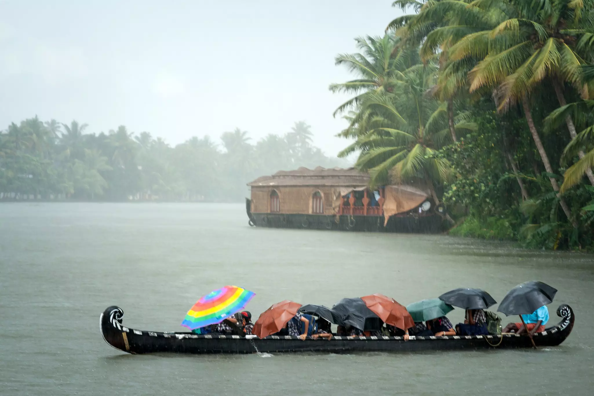 Monsoon time in the Kerala backwaters, with people crossing a river by boat in rain with umbrellas.
