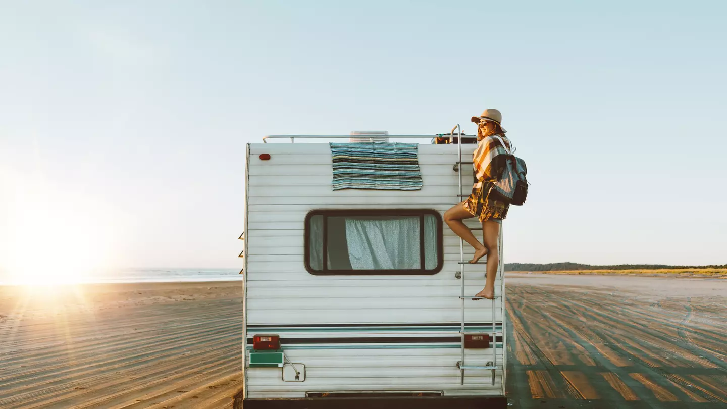 Young woman on the back of an RV, which is parked on the beach during sunset